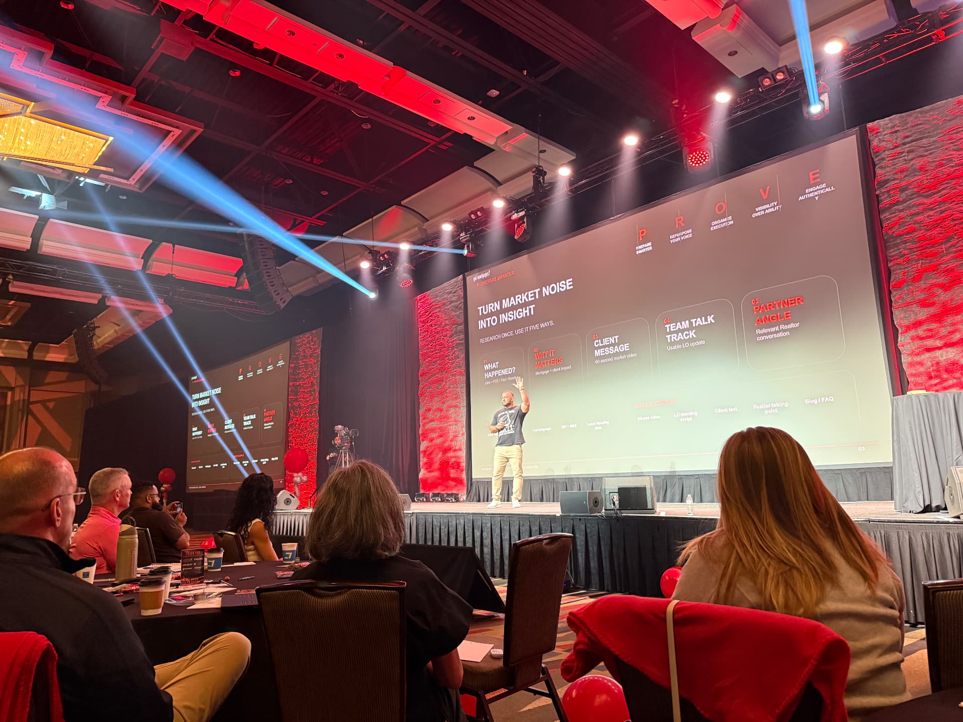 Keynote speaker on stage addressing a conference audience seated at round tables